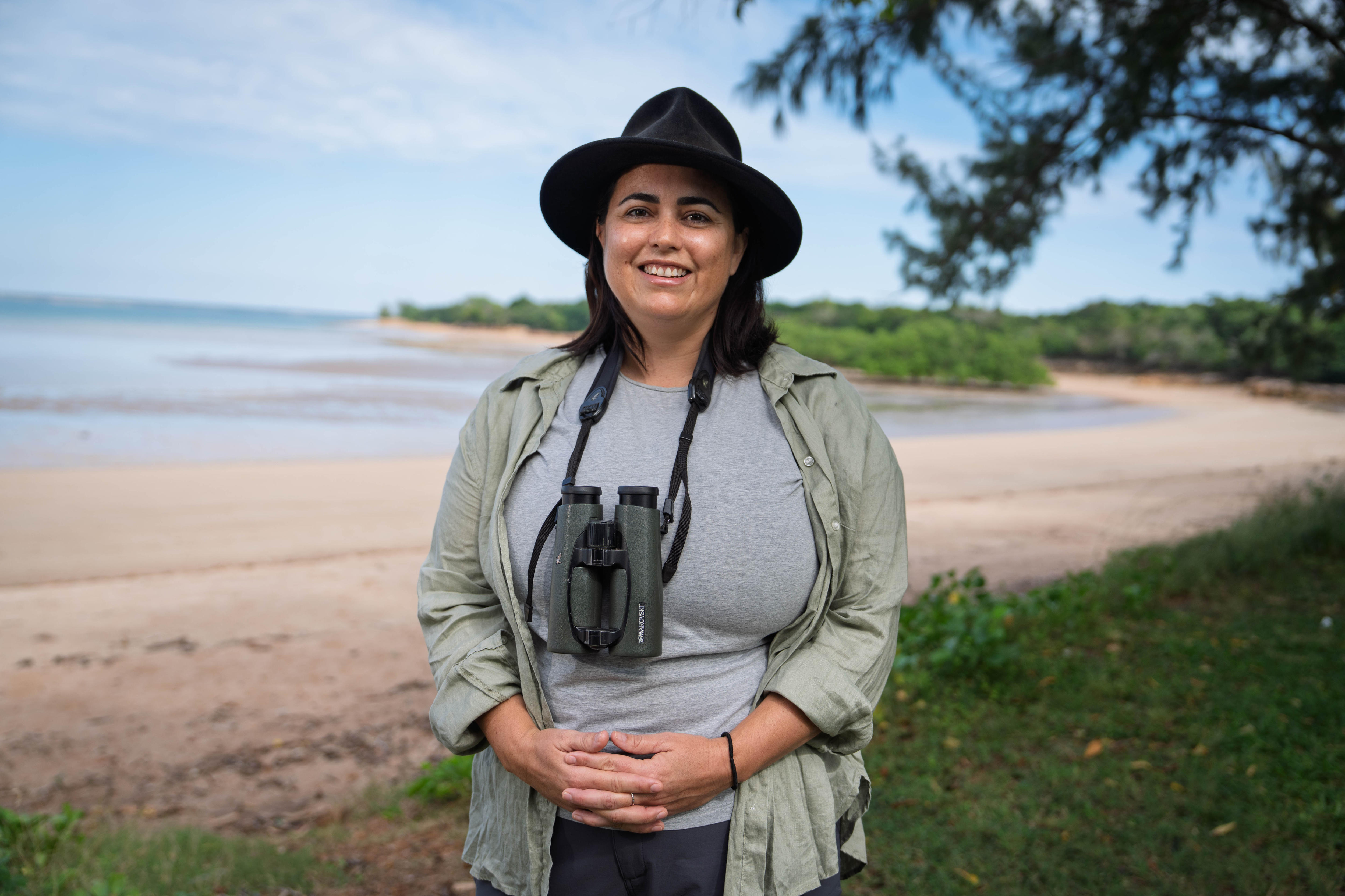 Una mujer con un sombrero de ala ancha lleva unos binoculares colgados de un cordón alrededor del cuello.