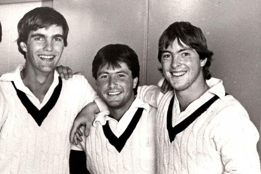 Four men in cricket whites pose for a photo.