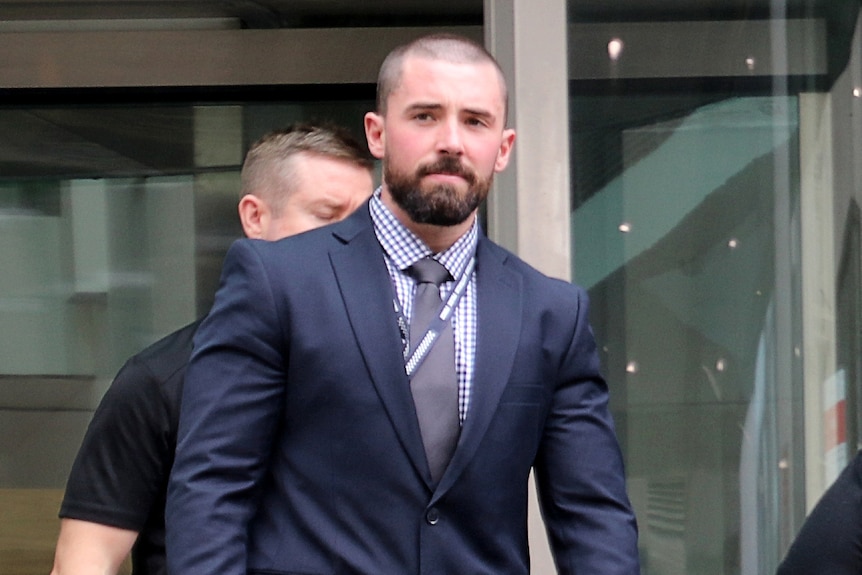 A police officer dressed in a blue suit walks out of a court building