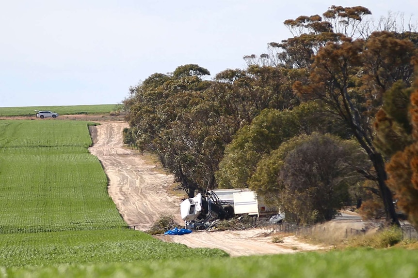 The wreckages of a semi-trailer and a car lie on the side of a country road after a crash.