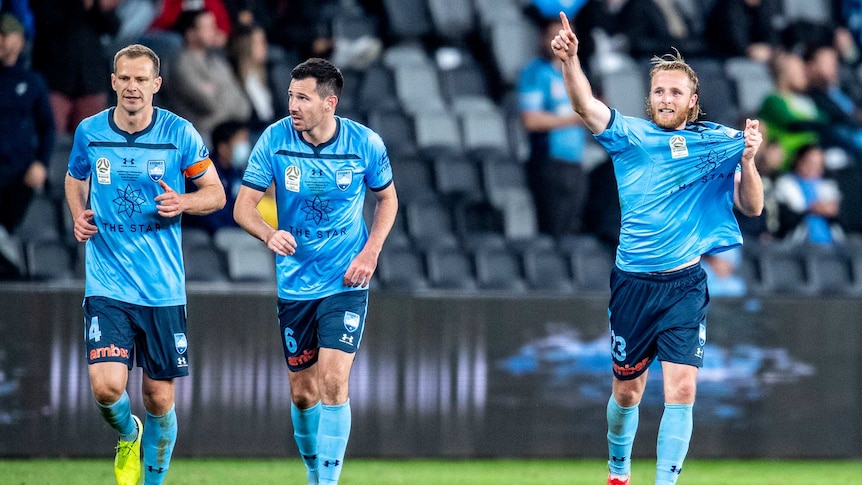 Rhyan Grant holds his shirt and points to the sky as two other players run next to him