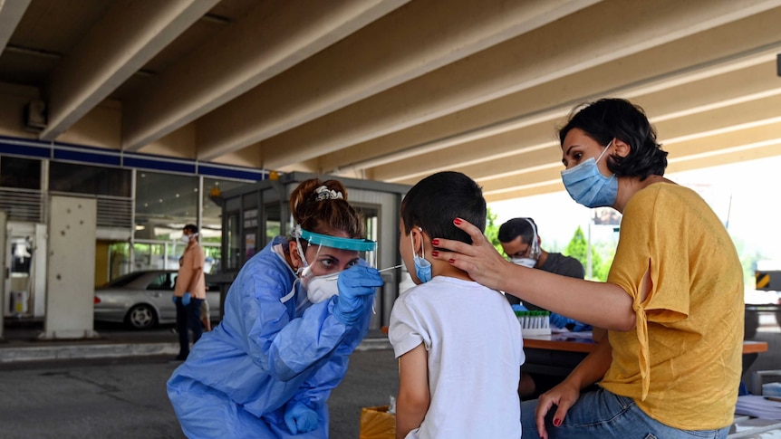 A health worker swabs a young boy's mouth as his mother comforts him.