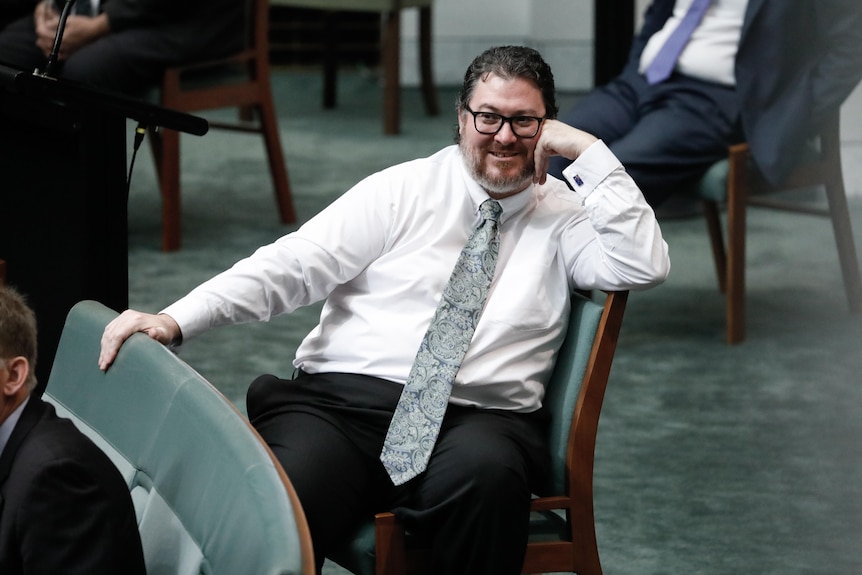 Christensen is sitting with a really long tie, no jacket, smiling, left arm resting on face.