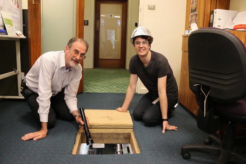 Michael Evans and Matthew Arnaudon kneel beside an access hatch to the tunnel at Old Parliament House.