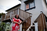 A woman in a red dress standing at the base of stairs to a house that's approx 2metres off the ground.