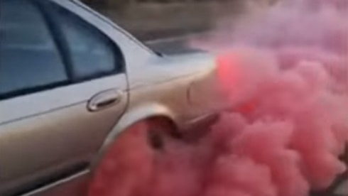 A car's back wheel billows pink smoke as it does a burnout.