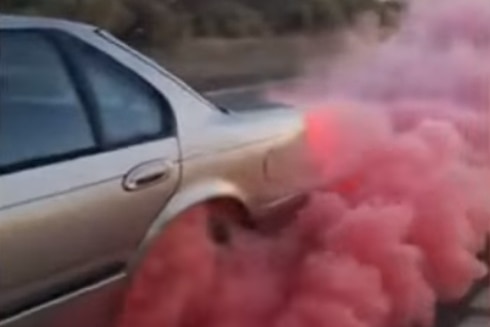 A car's back wheel billows pink smoke as it does a burnout.