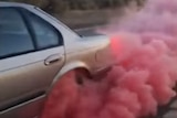 A car's back wheel billows pink smoke as it does a burnout.