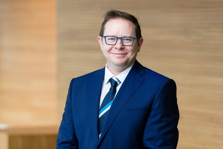 Dr Paul Griffin, smiles, while wearing a blue suit with glasses.