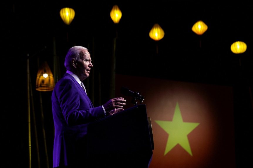 Joe Biden stands behind a lectern with a Vietnamese flag in the background. 