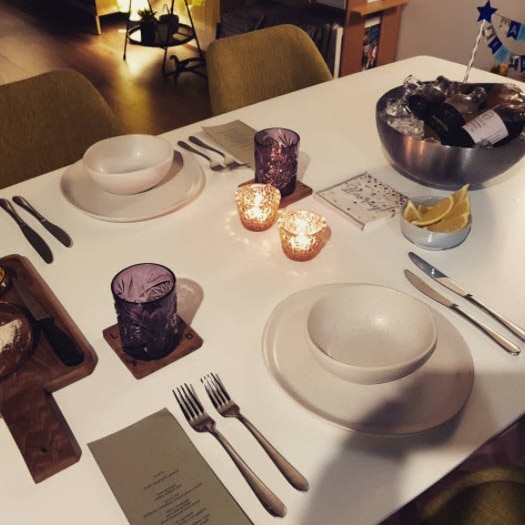A formal place setting with candles, menus and cocktails, on a white dining room table. 