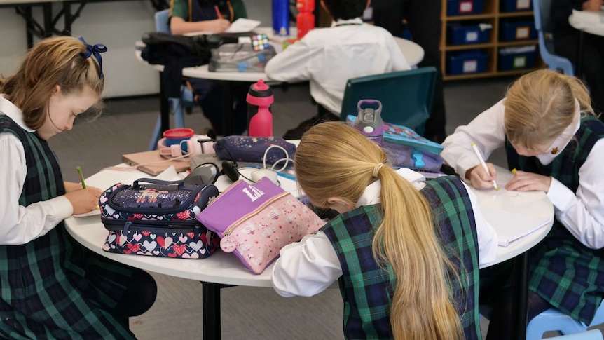 Children in school uniform sit at desks writing