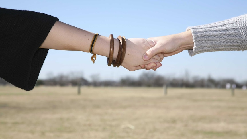 Two women hold hands across a field
