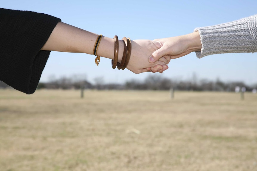 Two women hold hands across a field