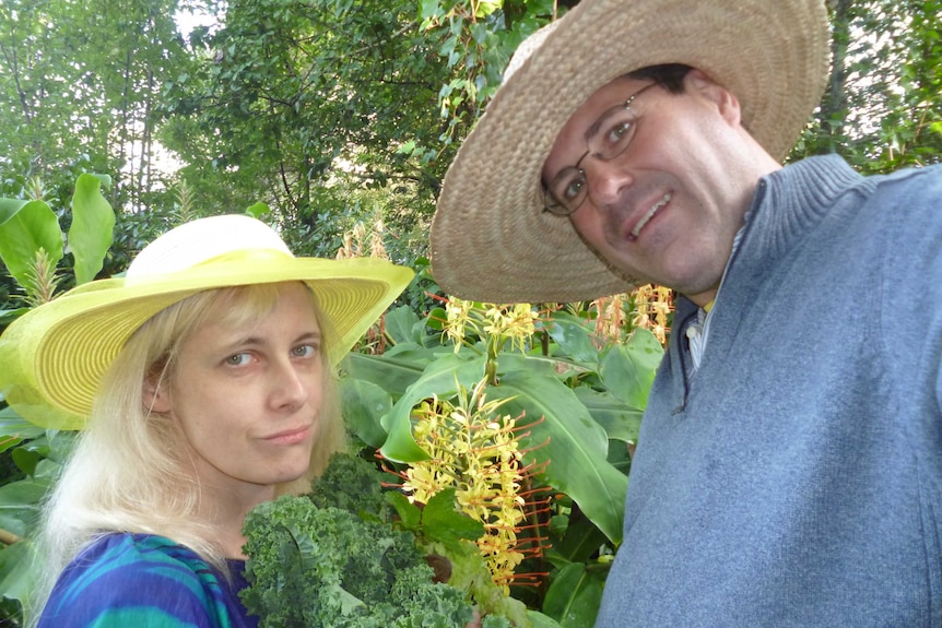 Two people wearing broad-brimmed hats standing in front of ginger lilies.