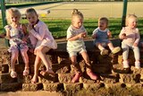 a group of young children sit in a row on a wall, eating.