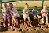 a group of young children sit in a row on a wall, eating.