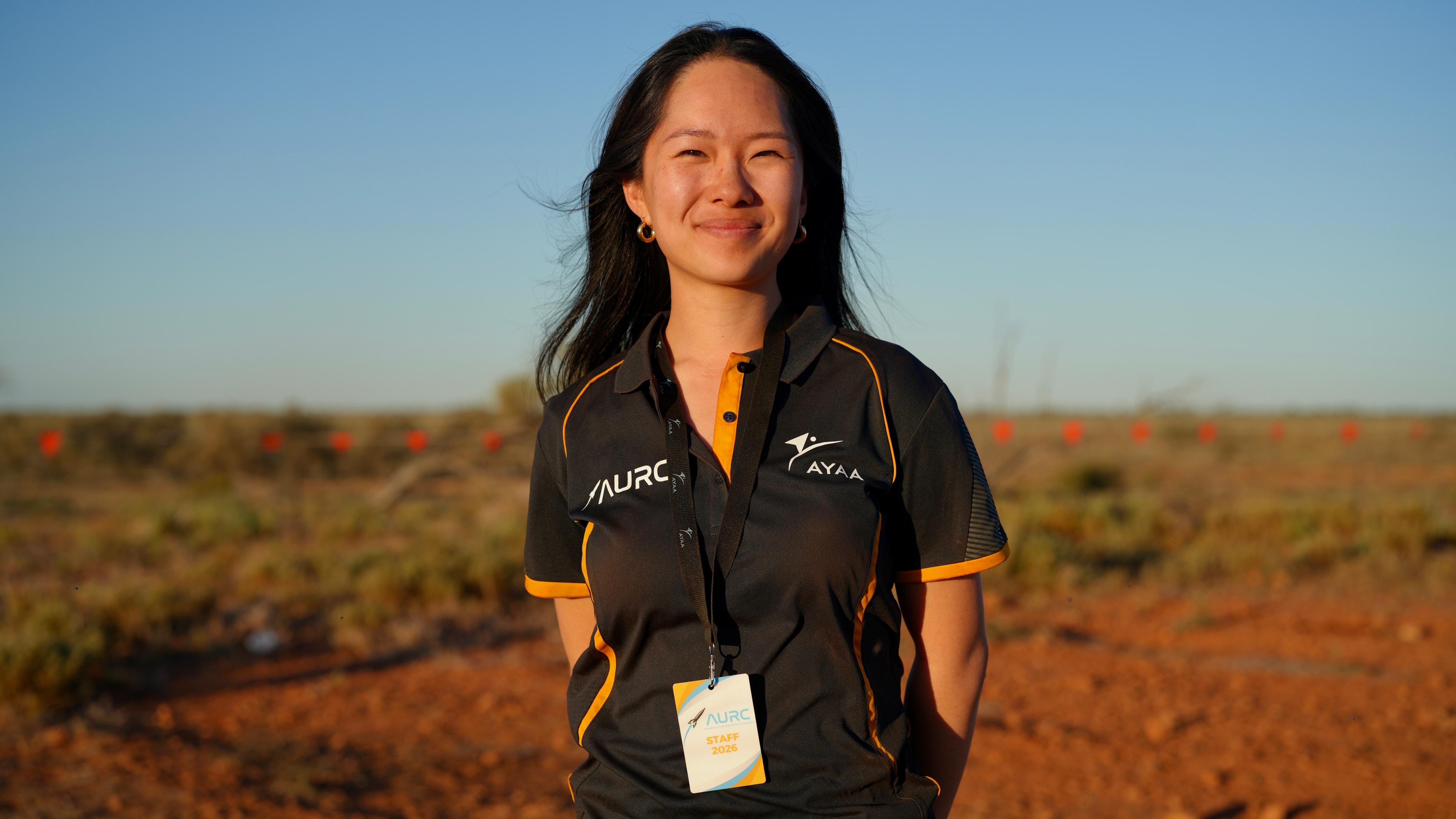 Jennifer He smiling at the camera in the red outback plains under a clear blue sky