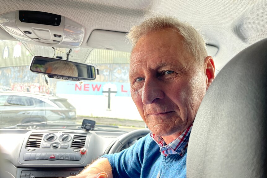 An older man in the driver's seat of a car looks over his shoulder to the back seat.