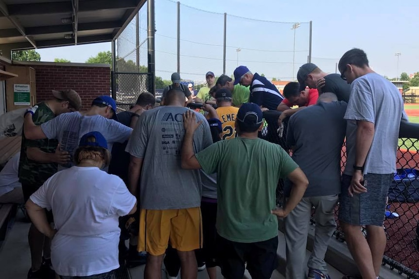 A group of Congress members and other join arms and pray next a baseball field.