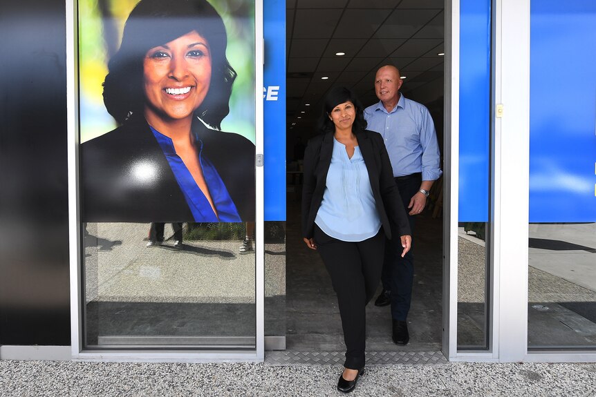 A woman and man walk out of a door way plastered in a picture of Roshena Campbell and liberal branding.