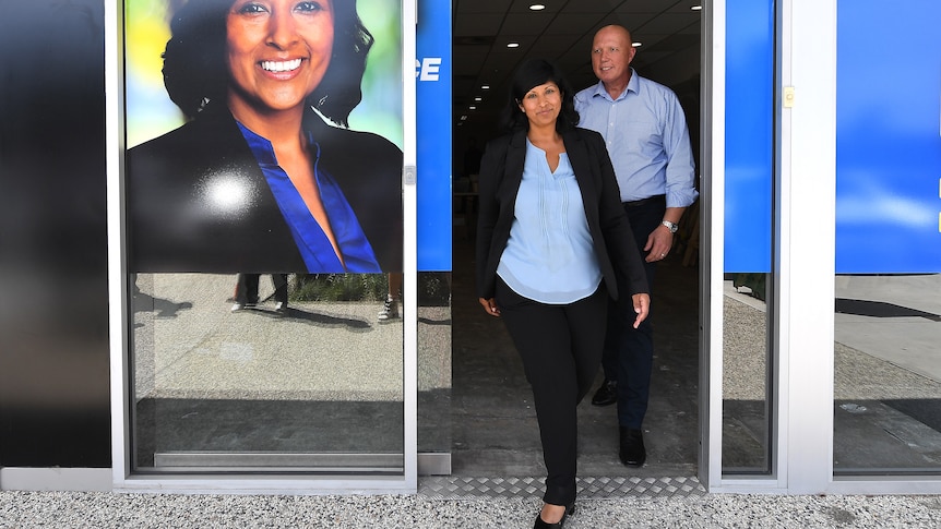 A woman and man walk out of a door way plastered in a picture of Roshena Campbell and liberal branding.
