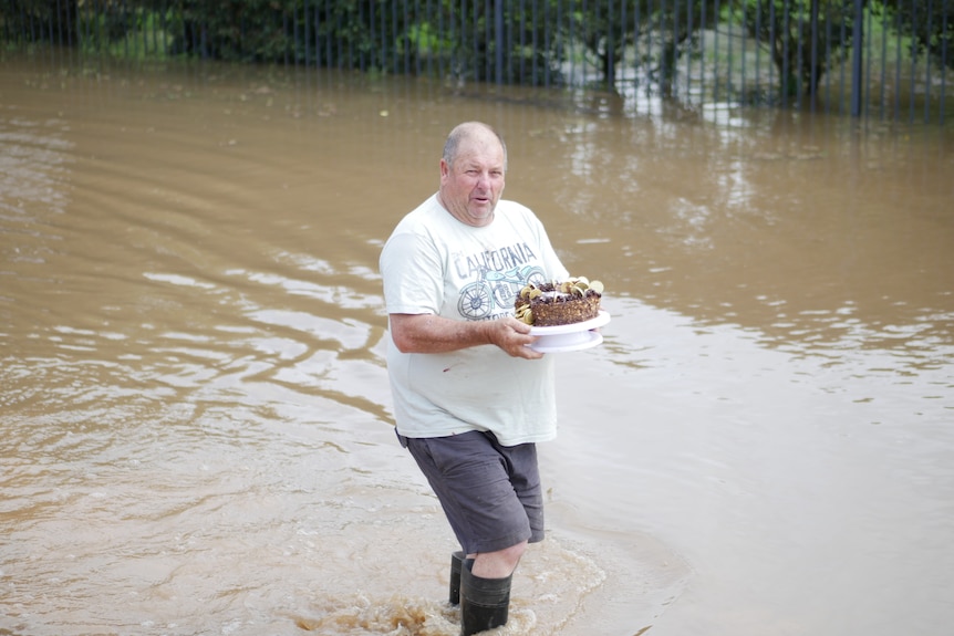 A man holding a birthday cake in a flooded street