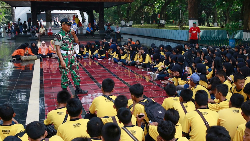Students listen to an army general at an outdoor forum at their school