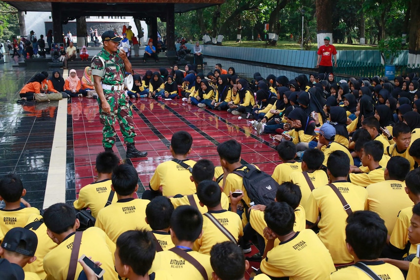 Students listen to an army general at an outdoor forum at their school