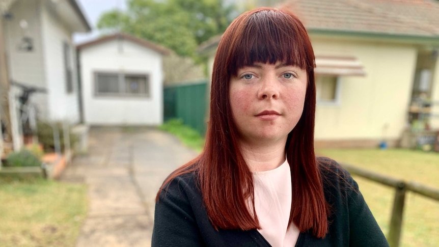 Sinead Simpkins stands outside a house and driveway, looking at the camera.