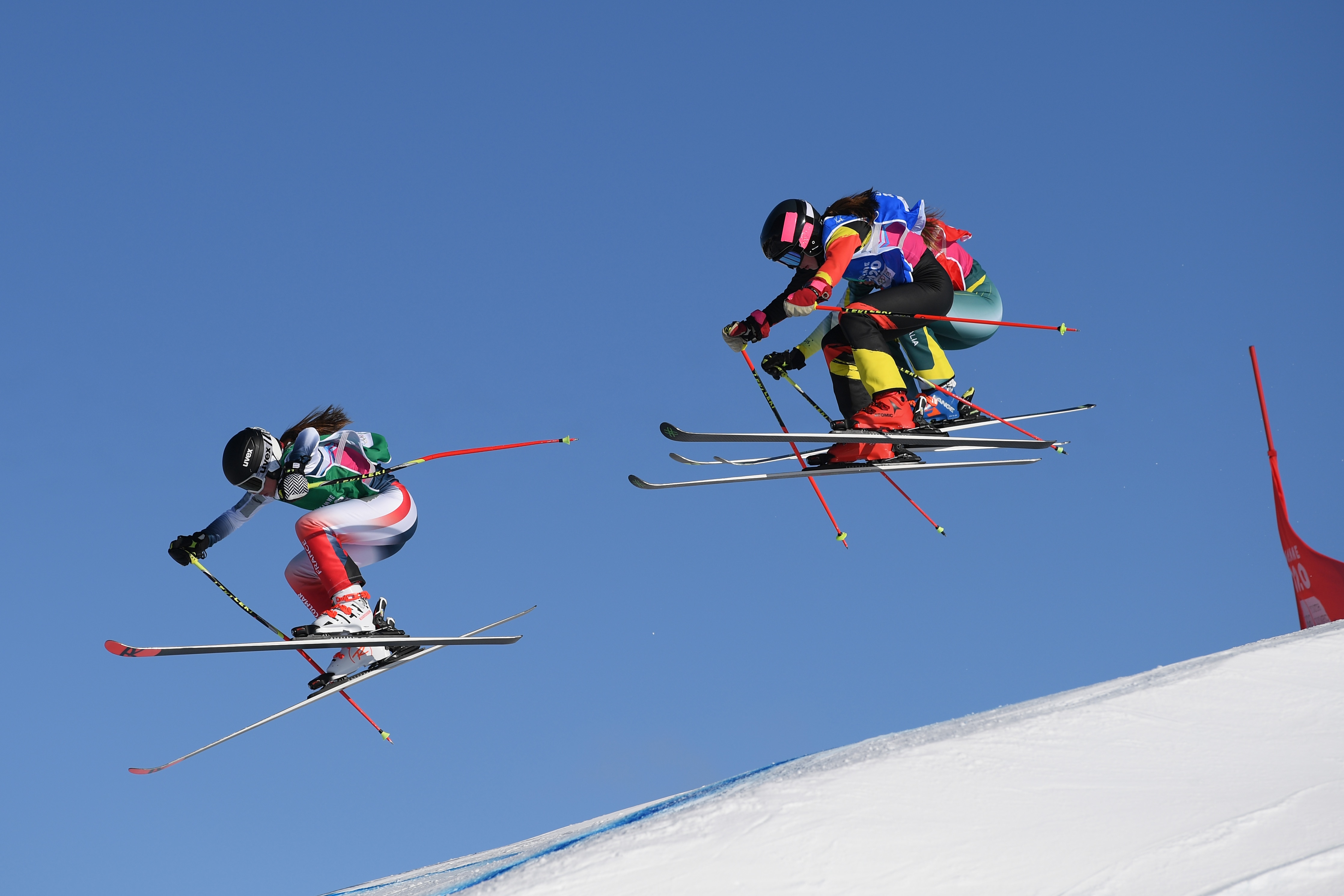 Three skiers leap over a jump