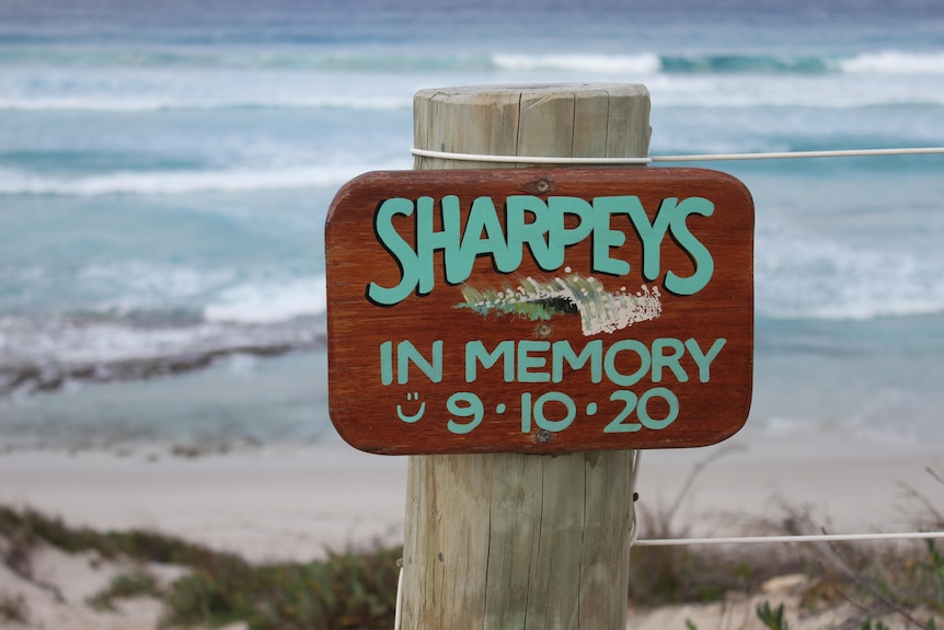 A small wooden plaque that says 'Sharpeys' with the beach in the background