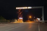 An illuminated sign for the Darwin Port sits over a road at night.