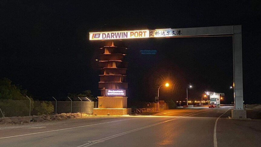 An illuminated sign for the Darwin Port sits over a road at night.