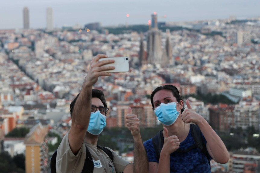 People wearing face masks take a selfie with Barcelona in the background