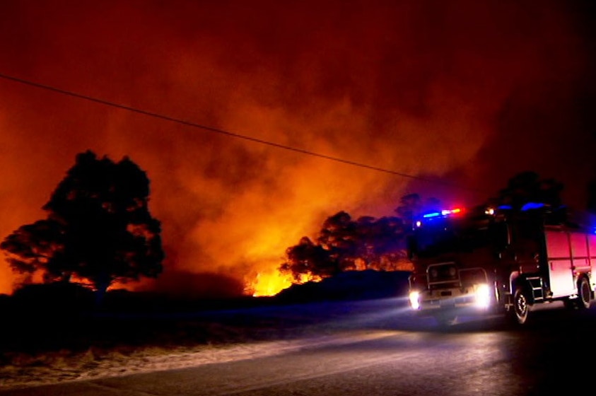 Un'autopompa parcheggiata sulla strada accanto a un incendio boschivo di notte a Stanthorpe.