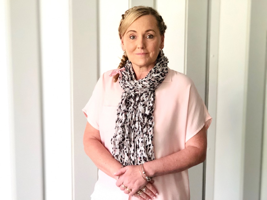 woman standing against a plain background, looking pensive.