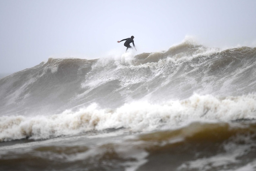 A man is surfing on a large wave the sky behind him is grey