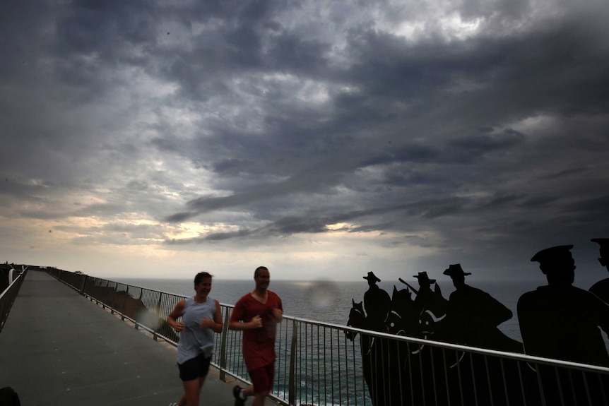Two men jog along Sydney's ANZAC walk at Bar Beach as ominous grey skies rage behind them.