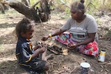 A child eating magpie goose with Children's Ground teacher Annie Ngalmirama.