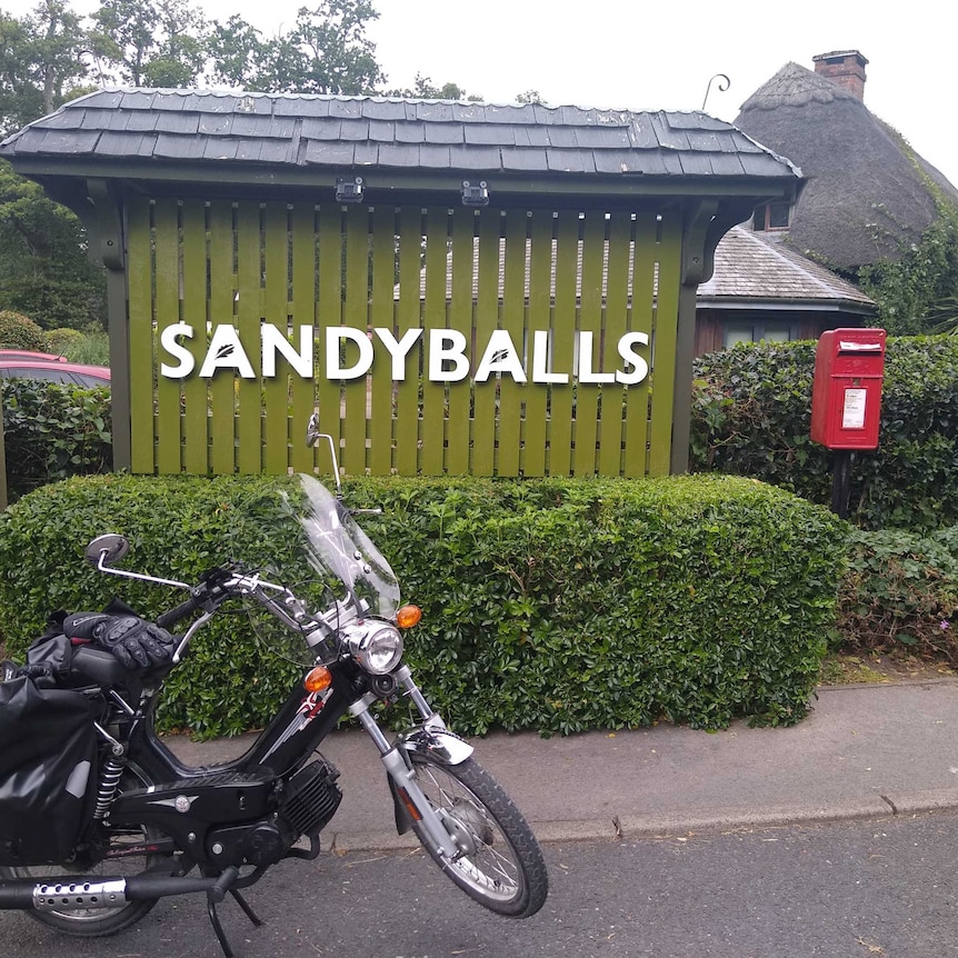 Paul Taylor's moped is parked in front of a large sign that reads, 'Sandyballs'.
