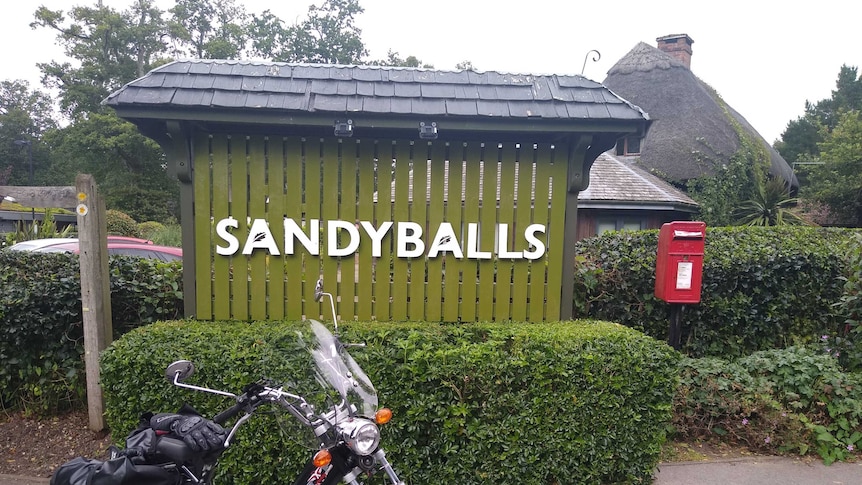 Paul Taylor's moped is parked in front of a large sign that reads, 'Sandyballs'.