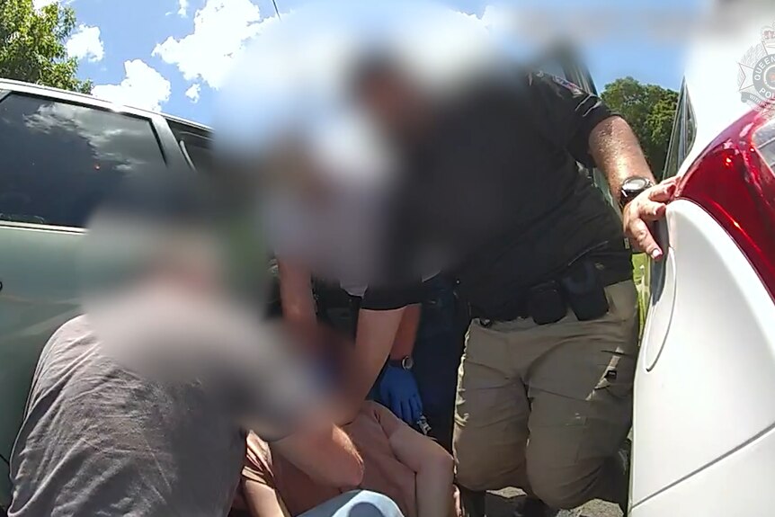 plain-clothes police officers arrest a man between two vehicles. everyone's faces are blurred