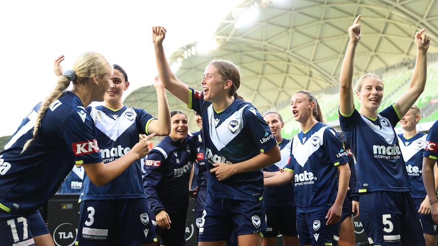 Melbourne Victory players celebrate together and gesture towards the crowd