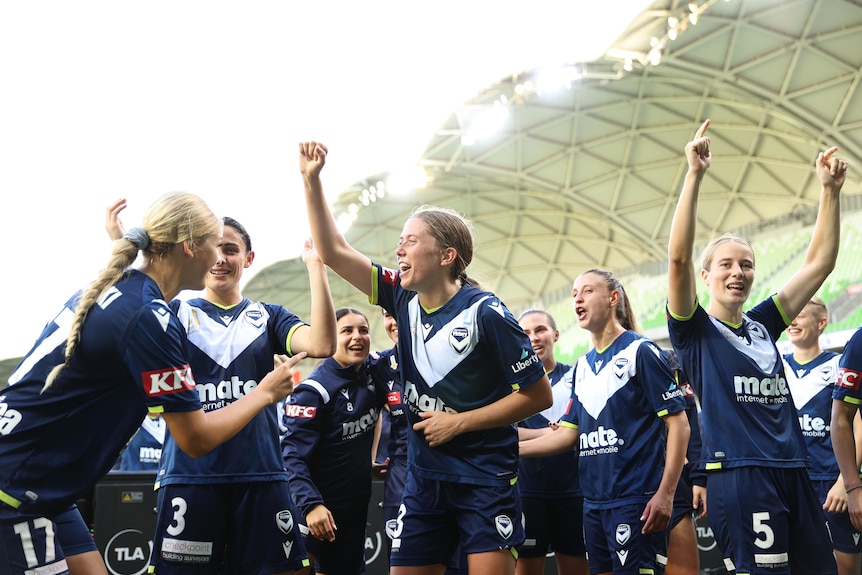 Melbourne Victory players celebrate together and gesture towards the crowd