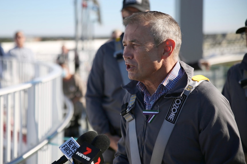 A tight head and shoulders shot of WA Deputy Premier Roger Cook wearing a safety harness and overalls.