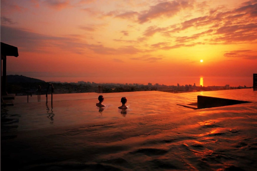 Two women sitting in an infinity pool-style onsen watch the sunset.
