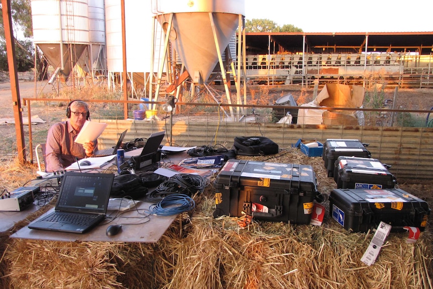 Tony Eastley broadcasts from a desk made of hay bales in Shepparton in 2013.