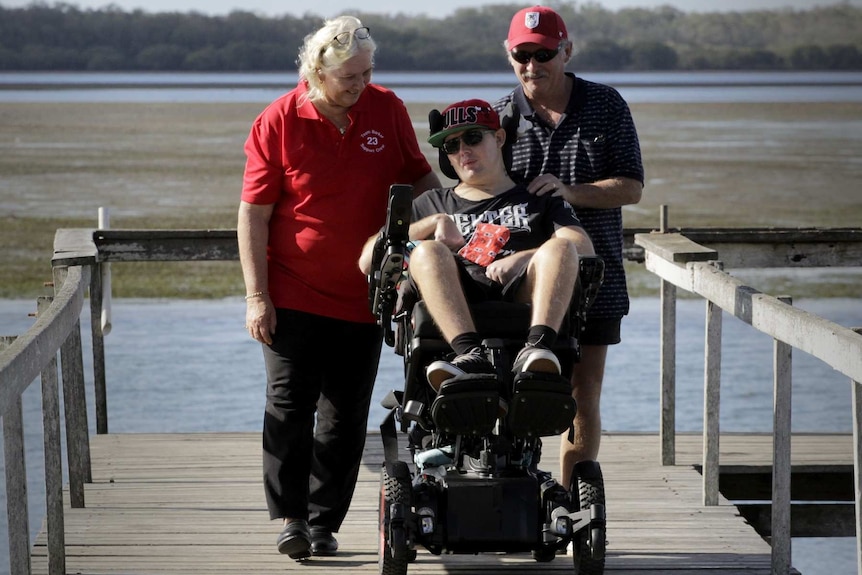 Chrys Barker is in a wheelchair while his parents Betty and Allan walk behind him.