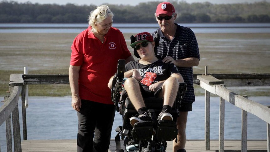 Chrys Barker is in a wheelchair while his parents Betty and Allan walk behind him.